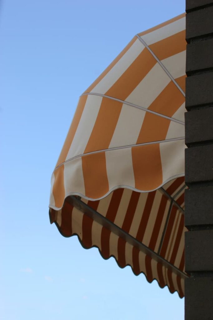 yellow-and-white-striped-window-awning-fully-extended-over-residential-window Yellow and white striped window awning fully extended over residential window